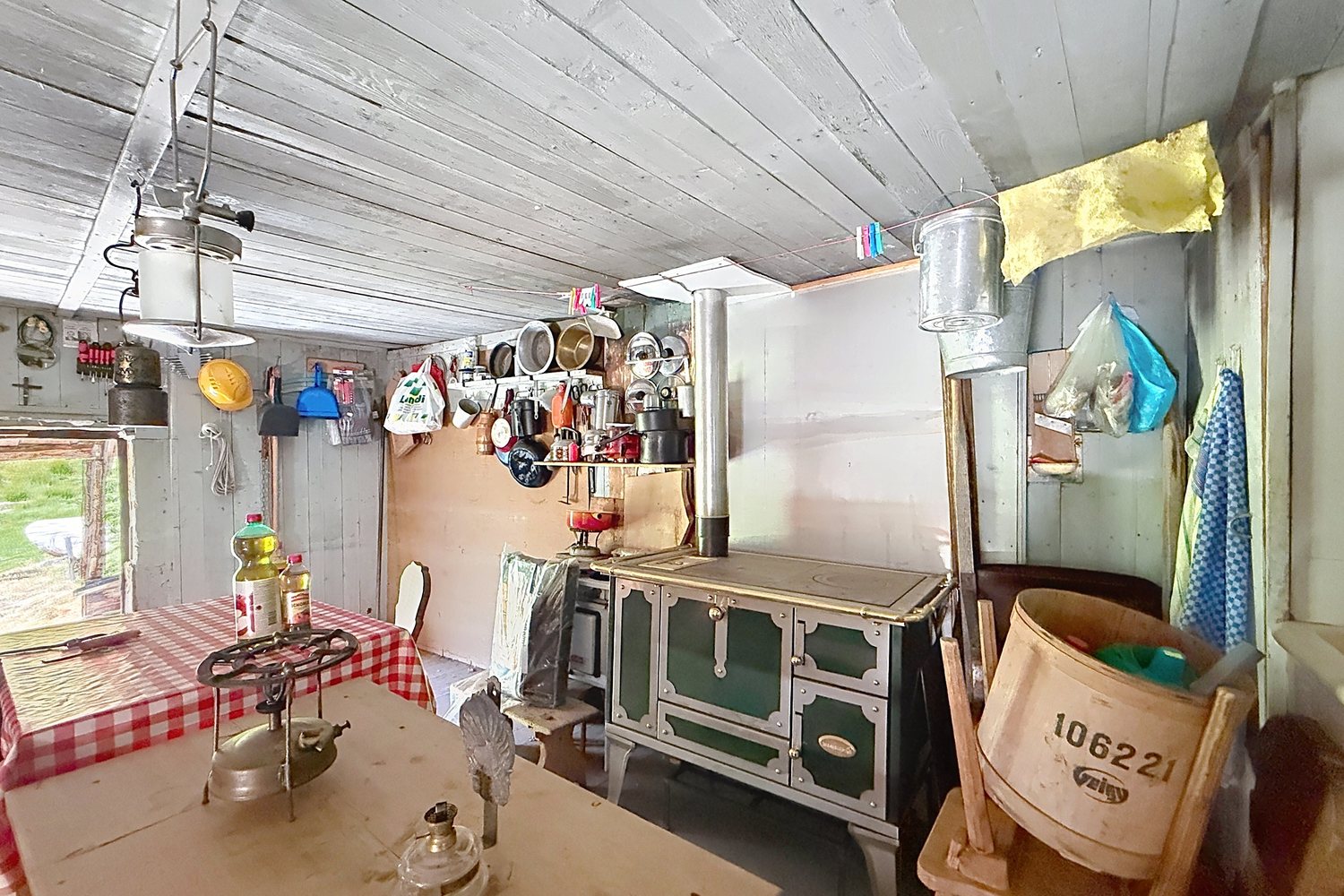Coin cuisine du mayen : fourneau à bois émaillé, batterie de cuisine accrochée au mur, lampes à pétrole sur la table.